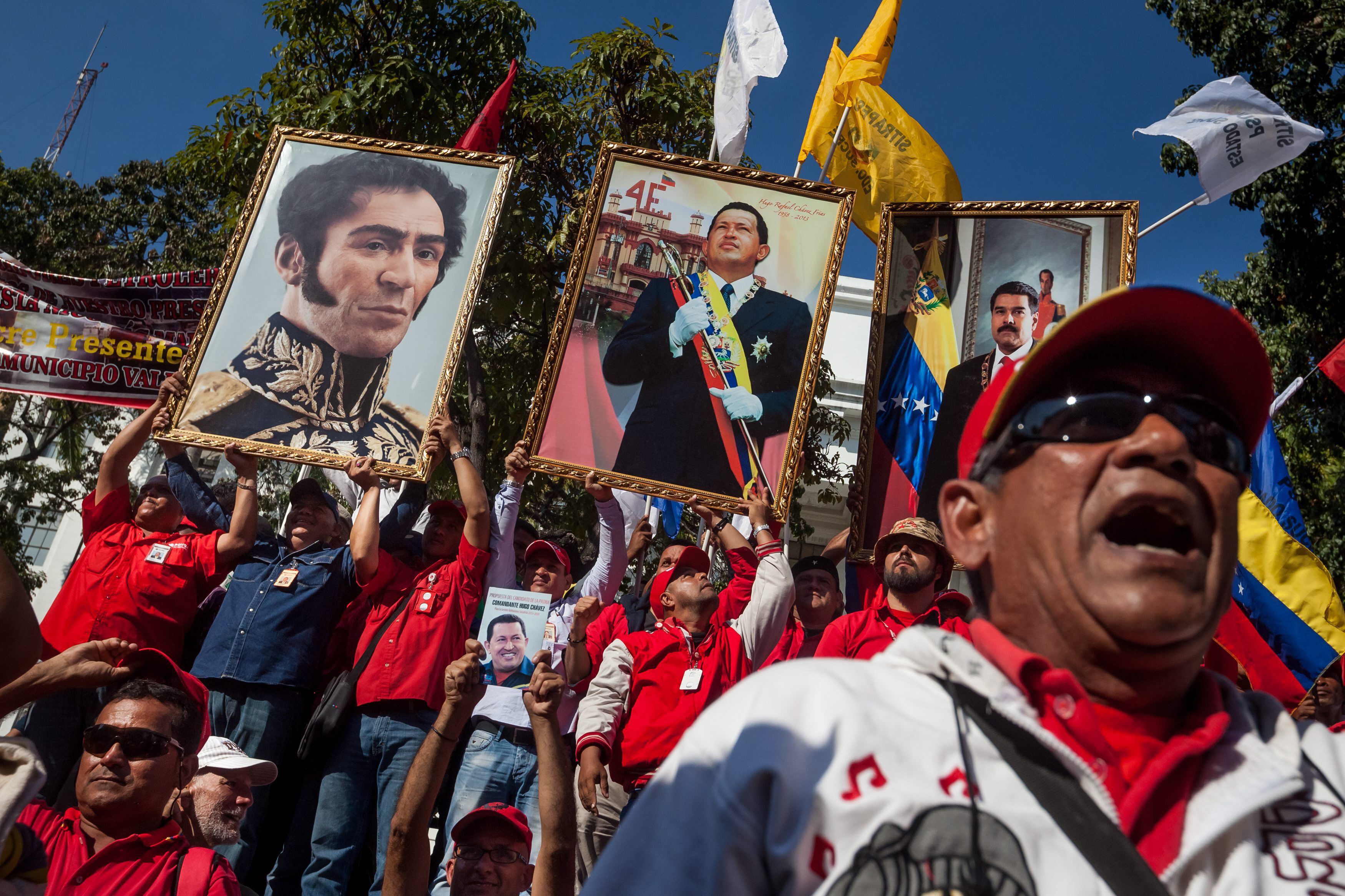 PDVSA workers march beneath banners depicting Simón Bolívar (left), the late President Hugo Chávez (centre), and Maduro. Photocredit: Shutterstock